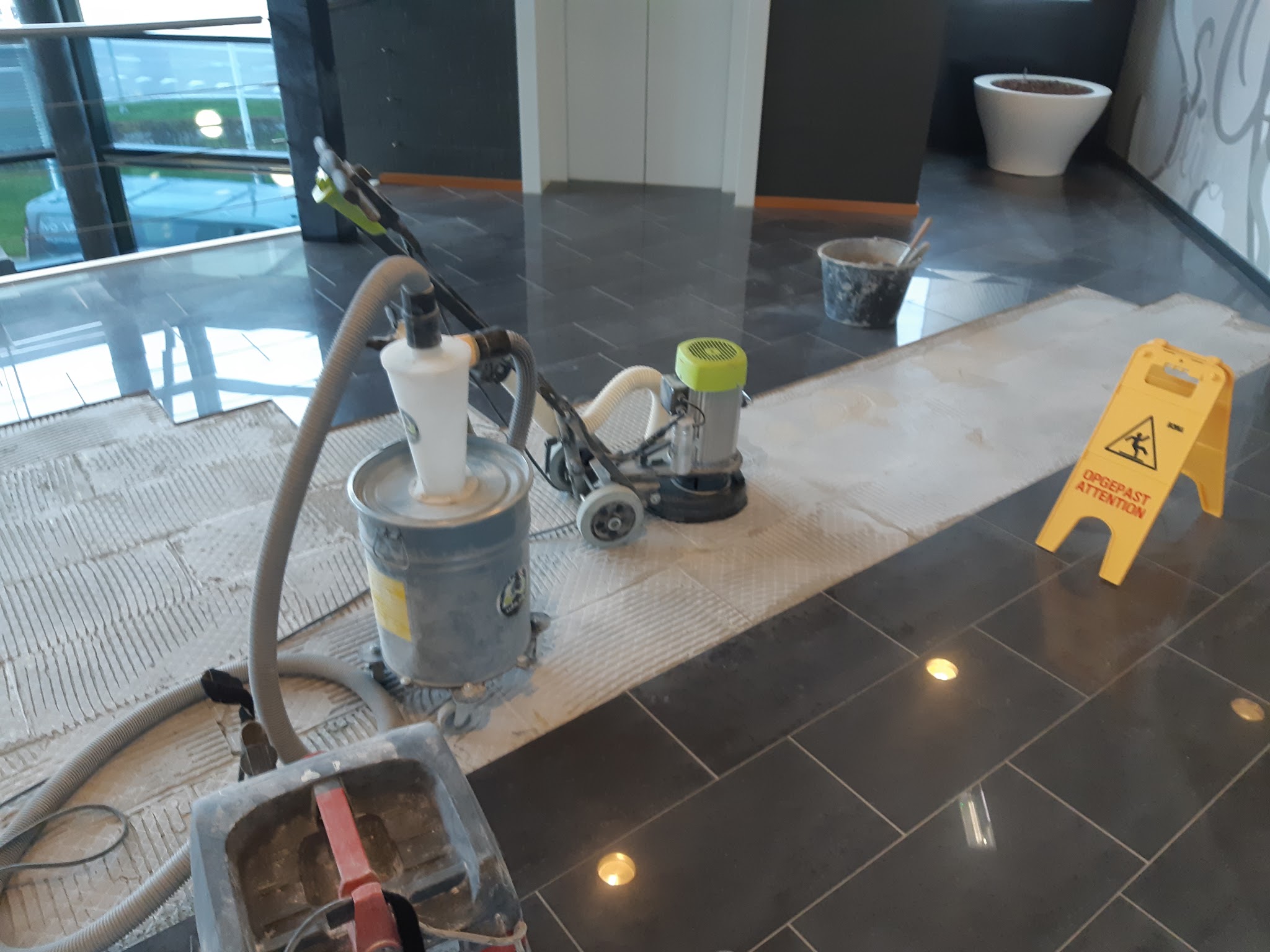 Het voorwerk aan een vloer, met schuurmachine en emmers, en een waarschuwingsbord