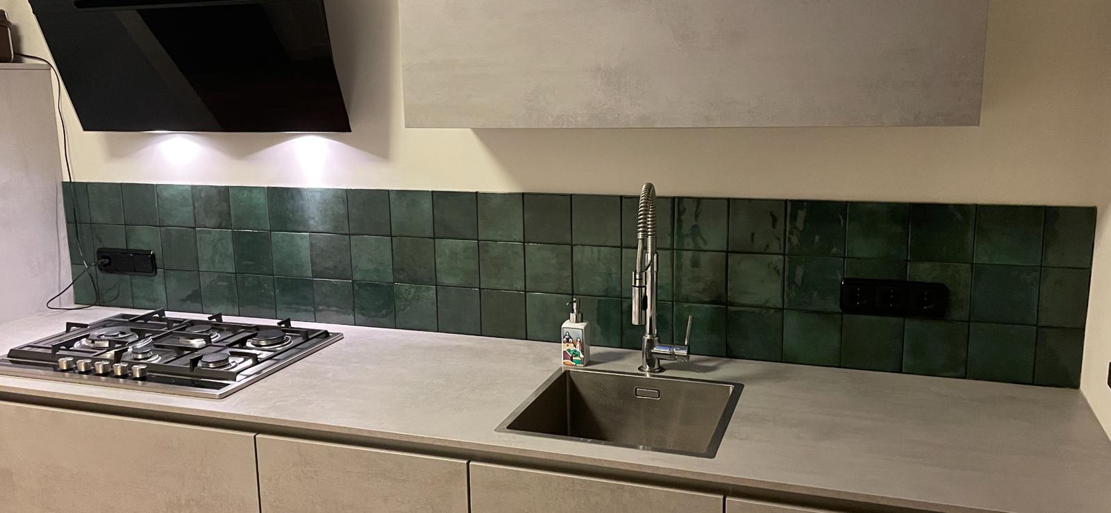 Smaragdgroene handvormtegels als spatwand in een keuken, boven een betonlook blad