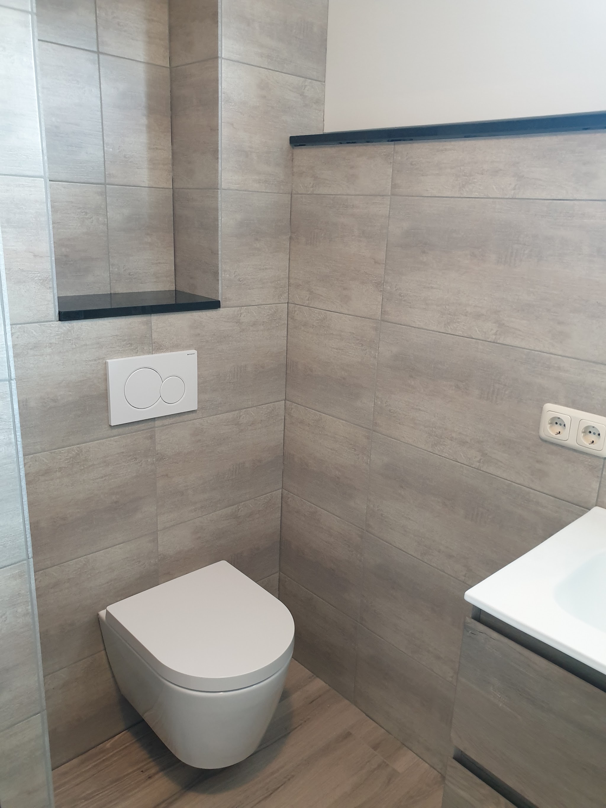 Betegeld toilet met een nis met zwarte hardstenen legplank en een houtlook vloer